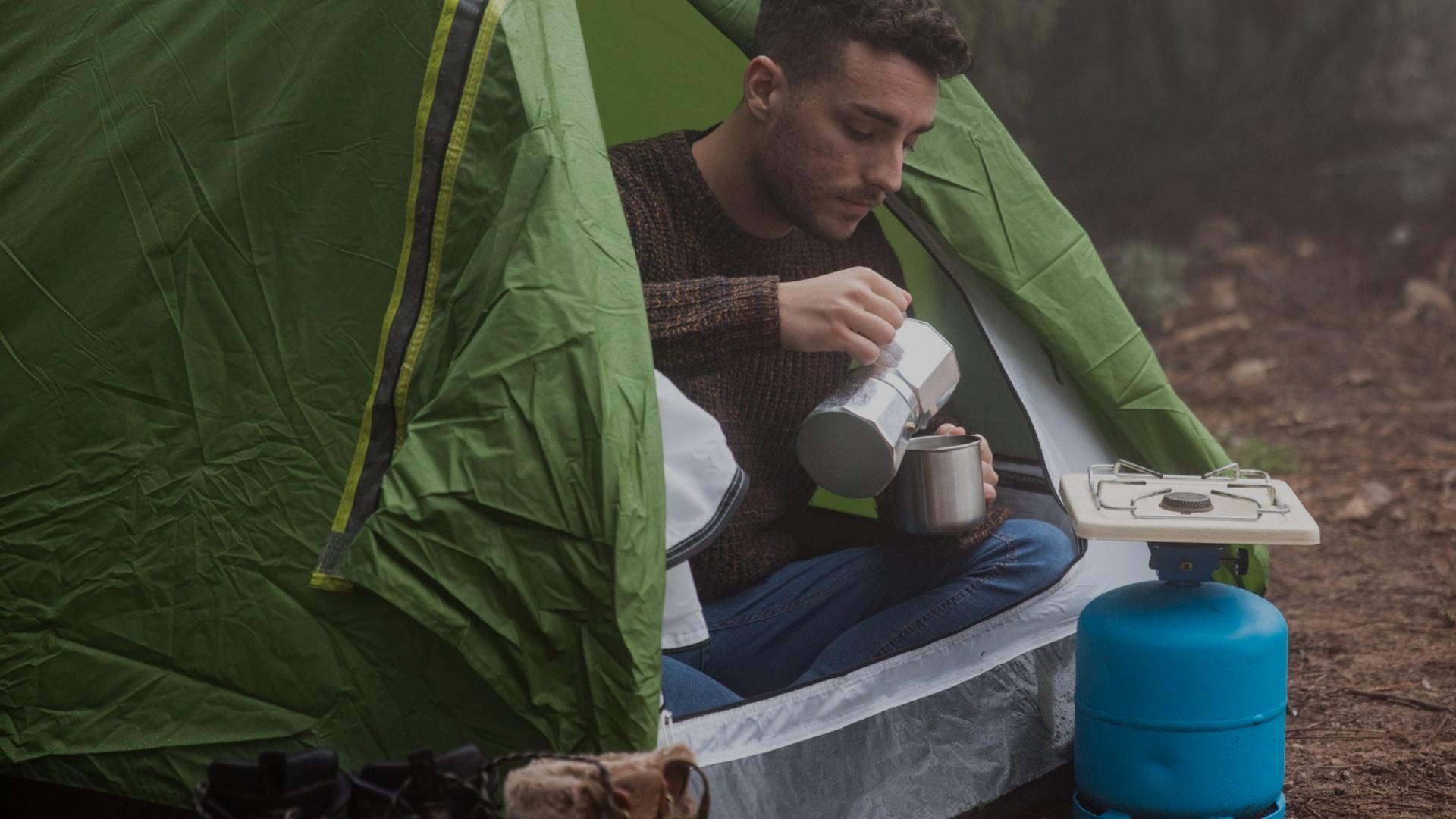 Man camping in a green tent, using a portable stove.