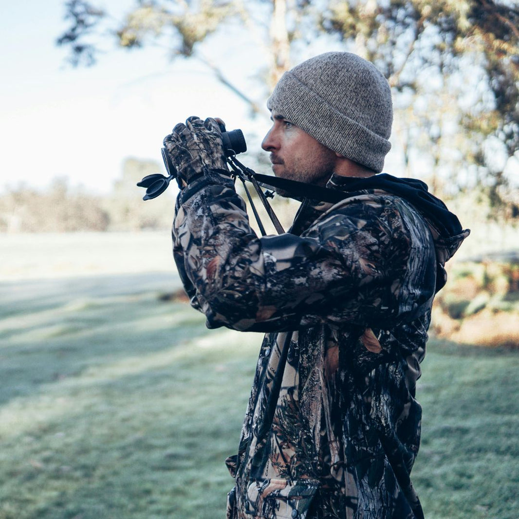 Person in camouflage clothing using binoculars in a natural setting