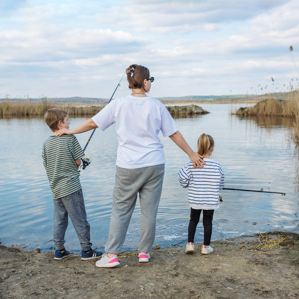 Woman and two children fishing by a lake on a cloudy day