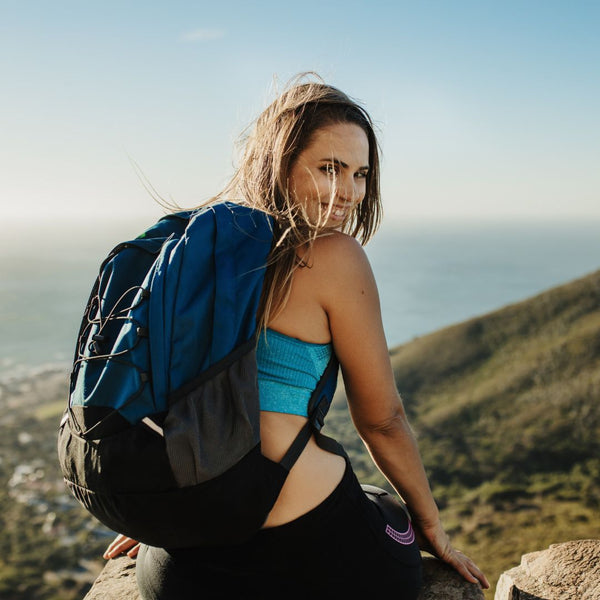 Woman with a blue backpack sitting on a rock with a scenic background