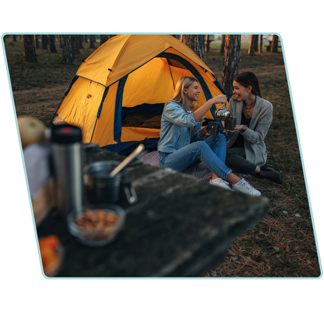 Two people sitting in front of a yellow tent in a forest setting.